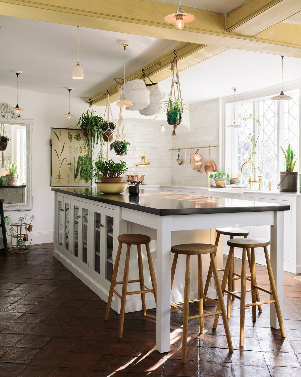 An oblique view of a Mediterranean-style classic kitchen with white painted cabinetry and an island with a dark hardwood worktop and four simple oak bar stools tucked into a breakfast bar end. TEST