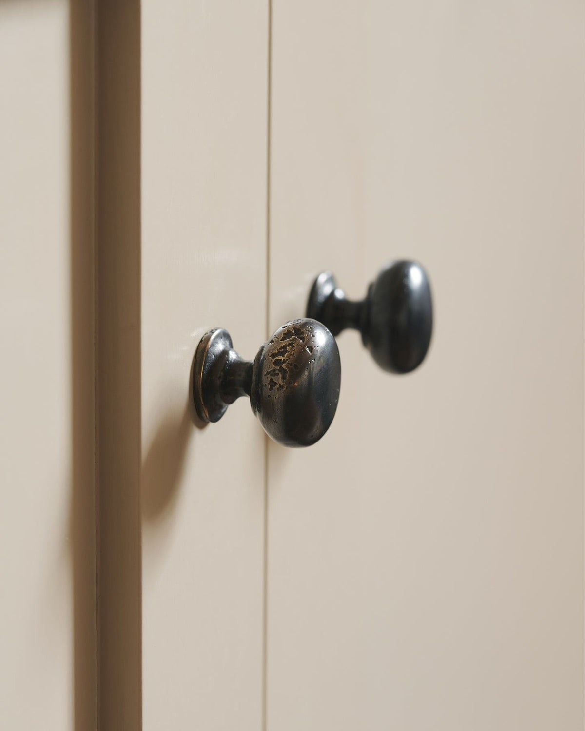 A close-up profile view of a pair of classic knobs in a dark oxidised bronze finish, fitted to a mushroom painted Shaker-style kitchen cupboard.|Medium shown TEST