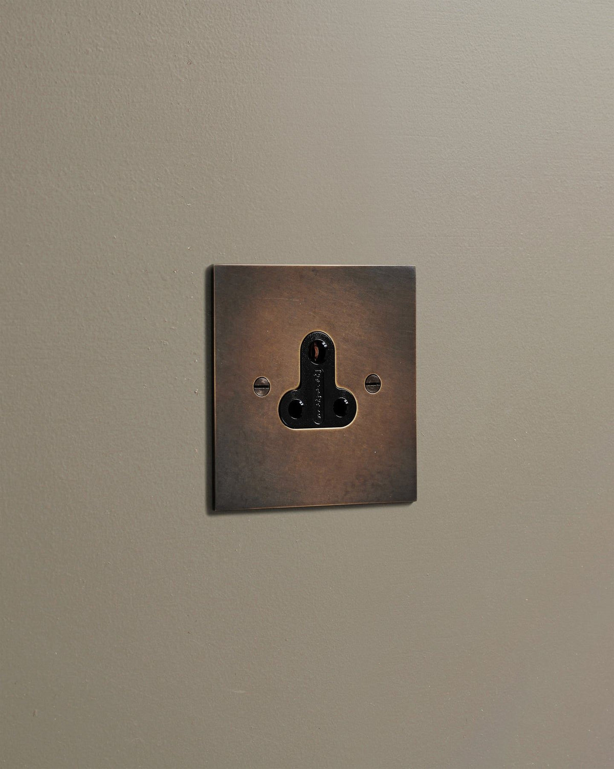 An oblique view of a classic 5 amp single plug socket in a dark oxidised brass finish. TEST