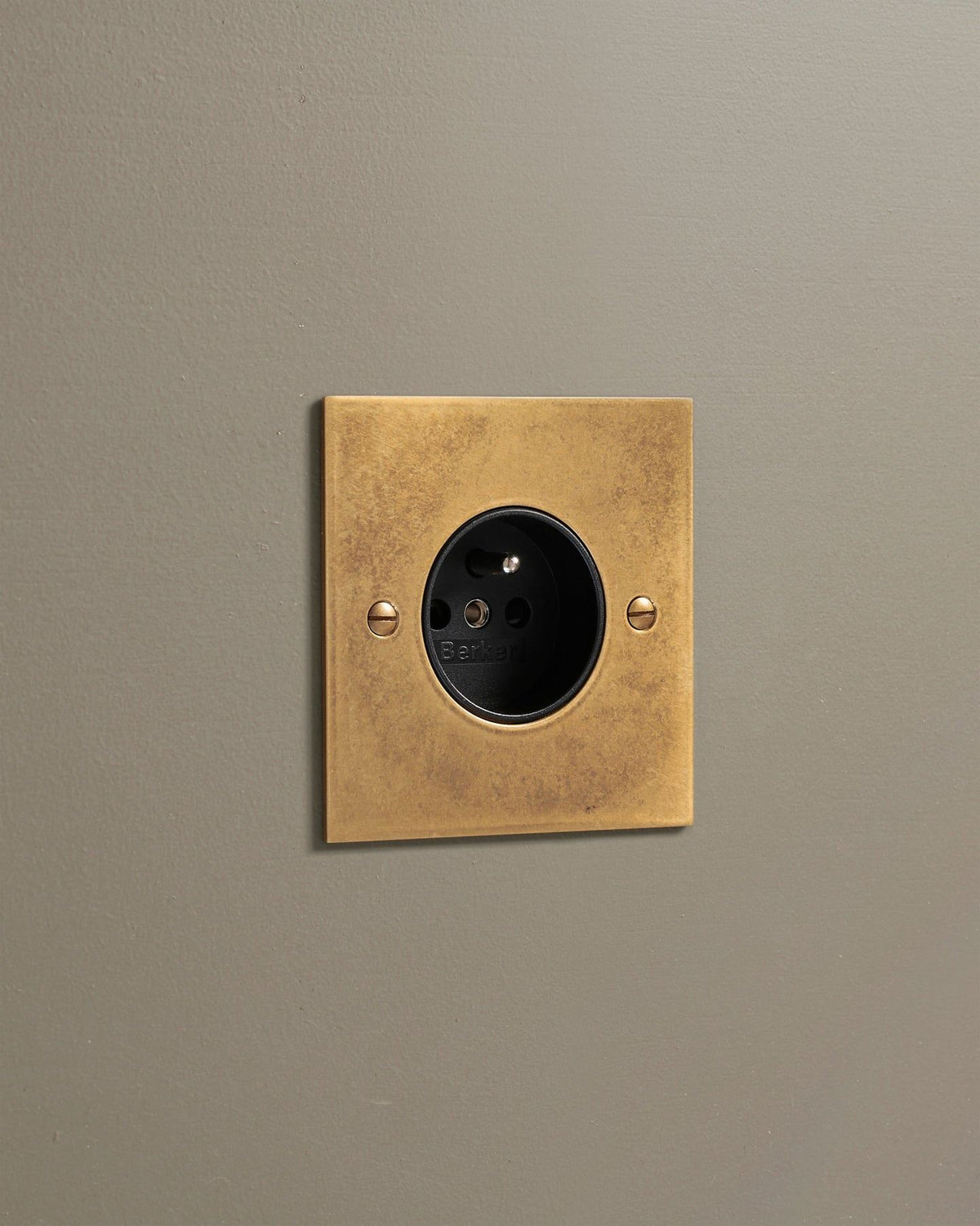 An oblique view of a classic French-style single plug socket in a mottled aged brass finish. TEST