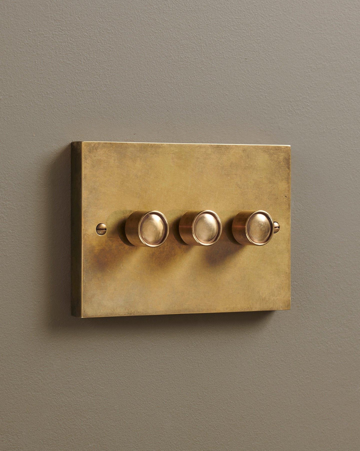 An oblique view of a 3 gang box dimmer switch in a warm burnished brass finish. TEST