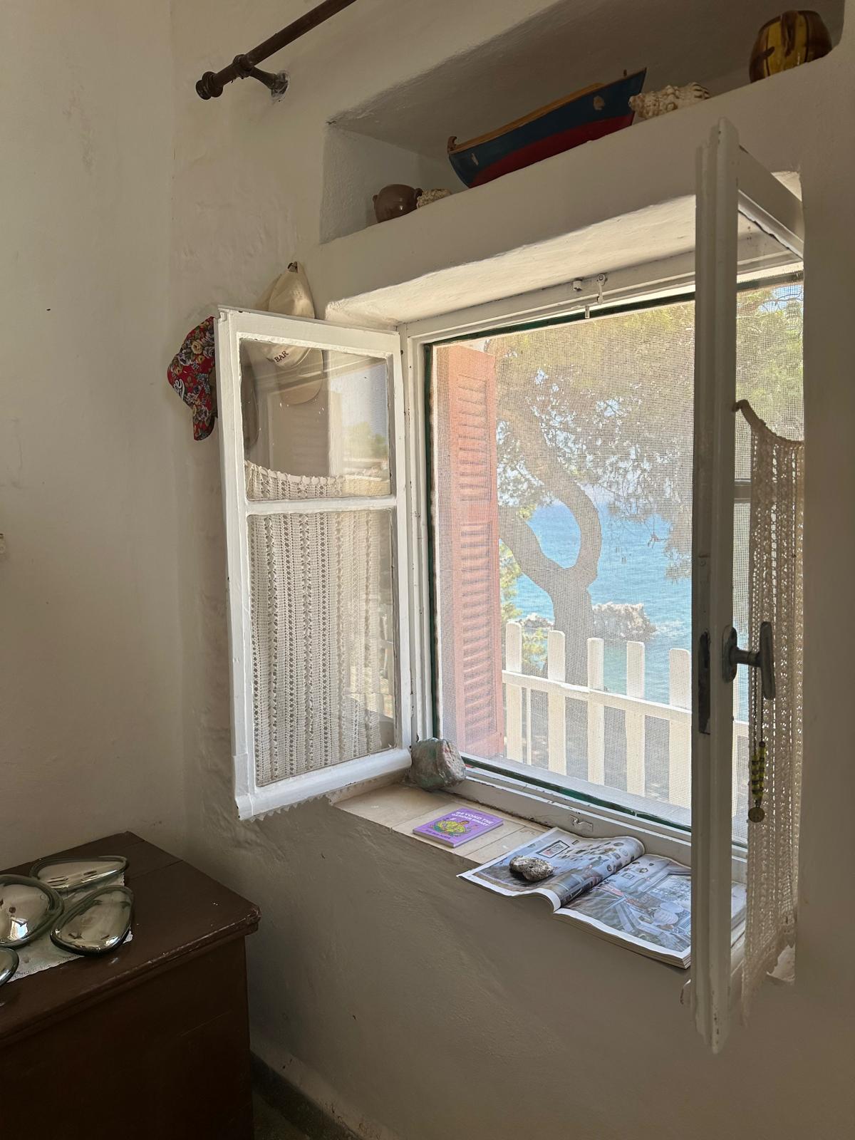 An open window in a simple home, the view is out to the ocean.