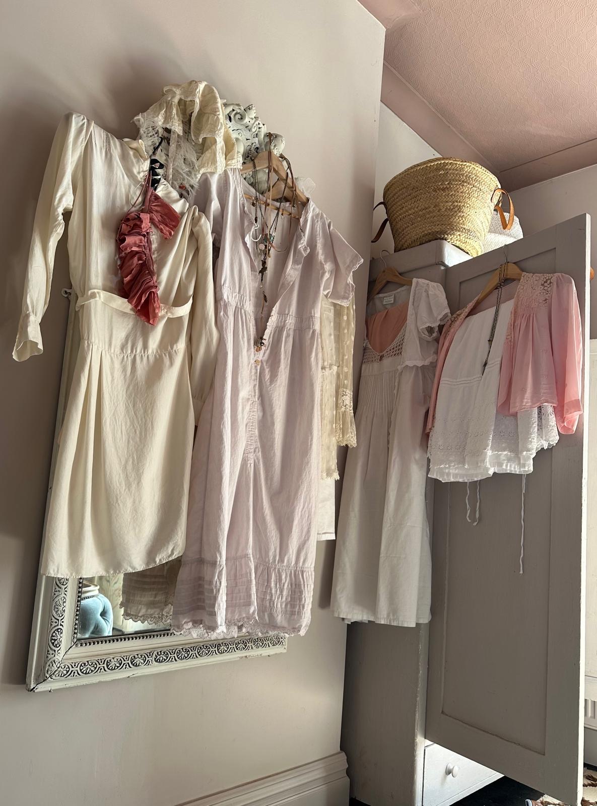 A selection of vintage-looking, pastel dresses hanging up on on a mirror and on a wardrobe door.