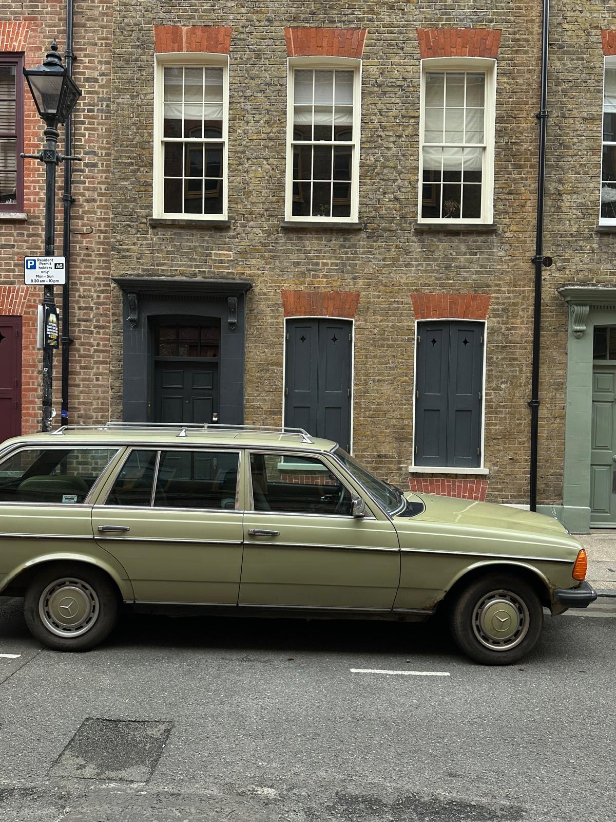 An old sage coloured car in front of a beautiful London townhouse with exposed bricks. The door and downstairs windows have been painted in a deep grey, the upstairs window frames have been painted white.