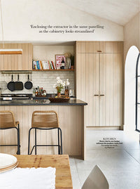 A page of a magazine, the full page is taken up by a photo of a kitchen. It has rough sawn timber fronts and the room is light and bright. There are two lines of text at the top of the page.