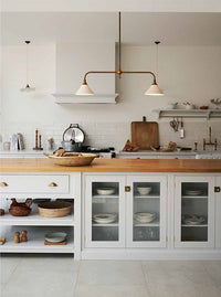 A page of a magazine, a photo of a white shaker-style kitchen covers the entire page. In the foreground is an island with glass-fronted base cupboards, an open section and an oak worktop. 