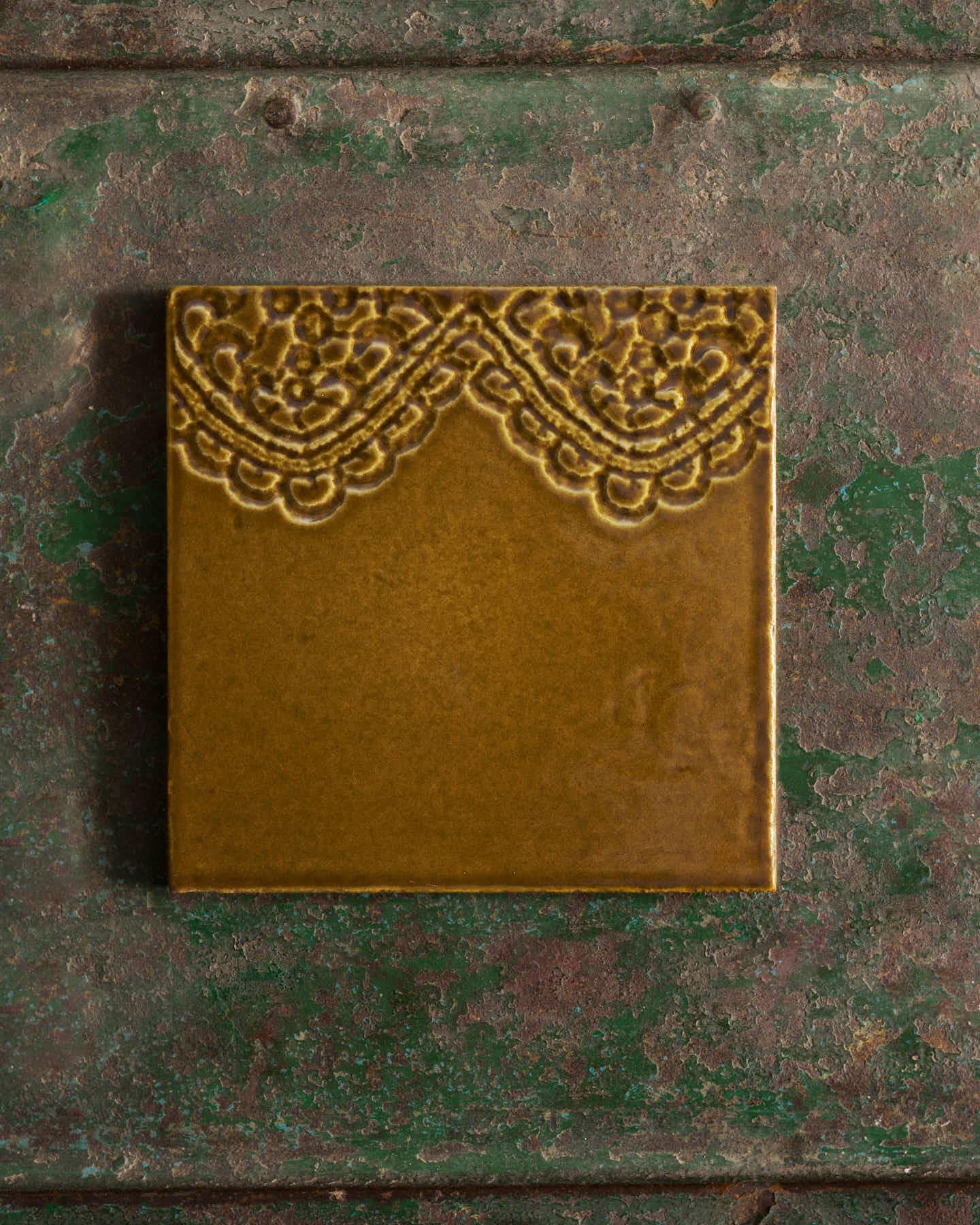Decorative sepia tile with lace pattern on a textured green surface.
