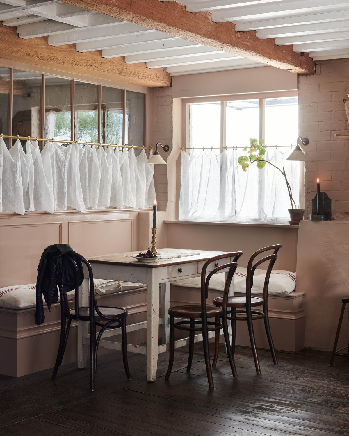 Dining area with wooden table and chairs, white curtains, and a window.
