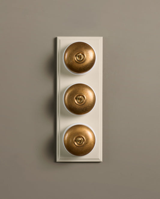 The Dolly Toggle Switch (3 Gang & Primed Maple Pattress) - Aged Brass with White Base.