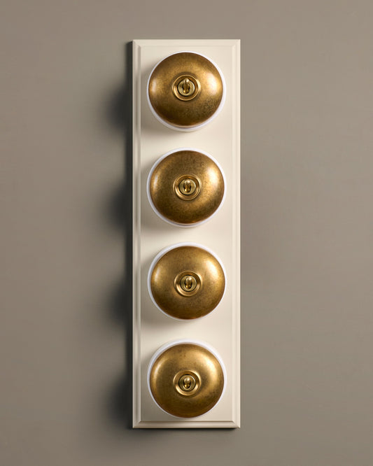 The Dolly Toggle Switch (4 Gang Row & Primed Maple Pattress) - Aged Brass with White Base.
