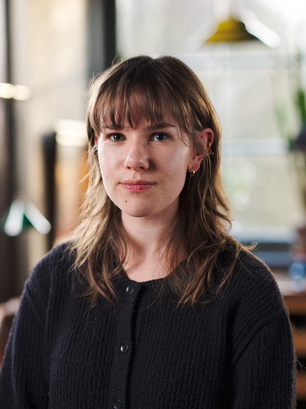 Woman with shoulder-length hair and bangs wearing a dark sweater indoors.