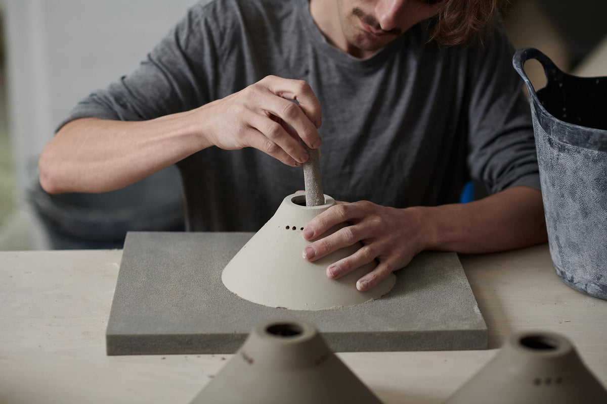 A ceramicist carefully cleaning up the edges of a dry porcelain lamp piece.
