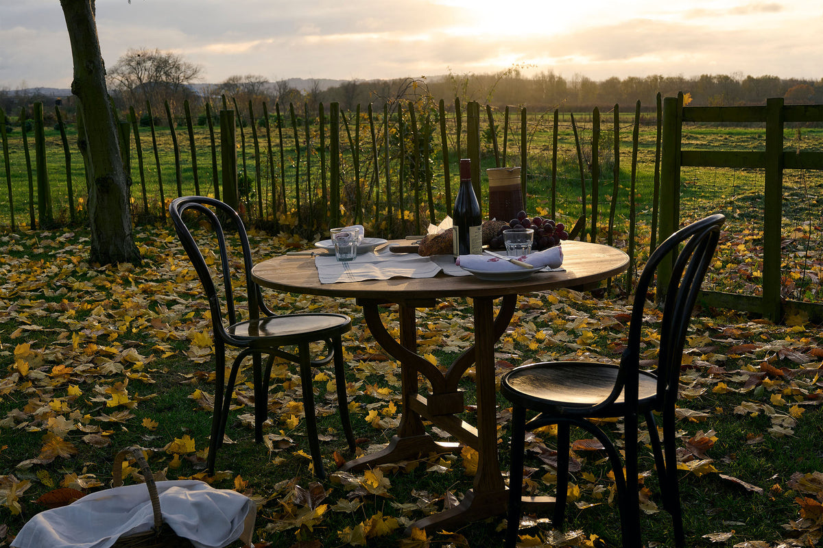 A vineyard table and two vintage café-style chairs outdoors on the grassy fields overlooking at sunset.