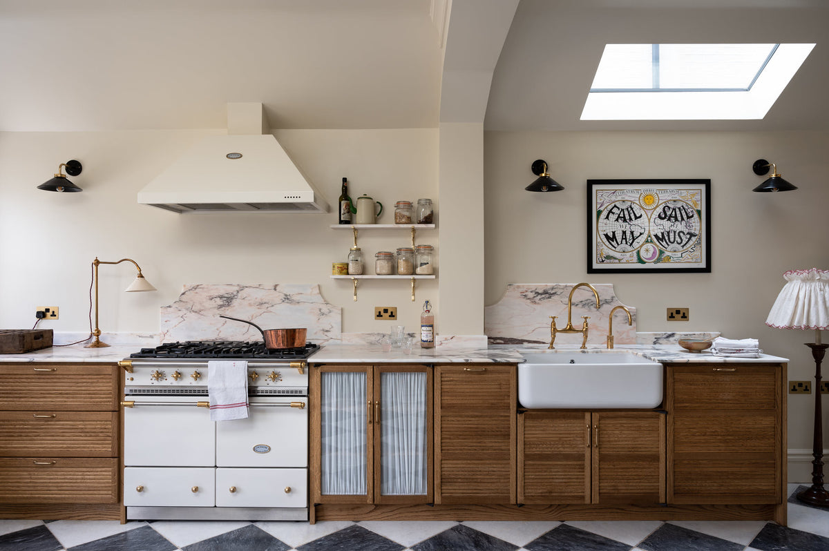 A beautiful white Lacanche cooker flanked by six impressive Haberdasher’s base cupboards, mostly closed with tactile tambour fronts except for a glazed double-door cupboard with delicate ethereal muslin curtains. Sandwiched between pale pink Paonazzo marble worktops and dramatic black and white marble flooring, this kitchen has a subtly luxurious feel.