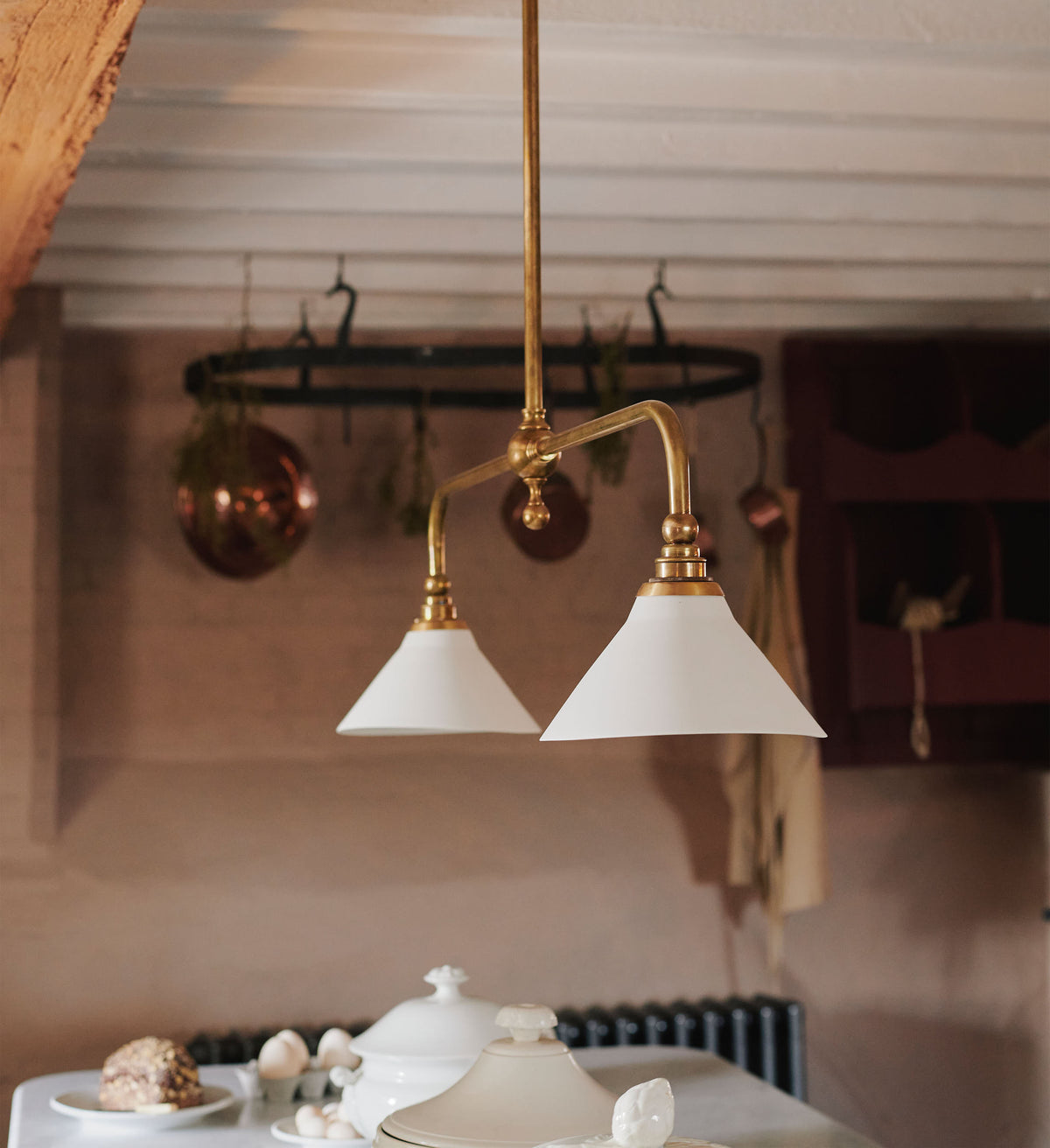An oblique view of the heirloom gaselier light, hanging on top of the heirloom dairy table with artisan ceramics.