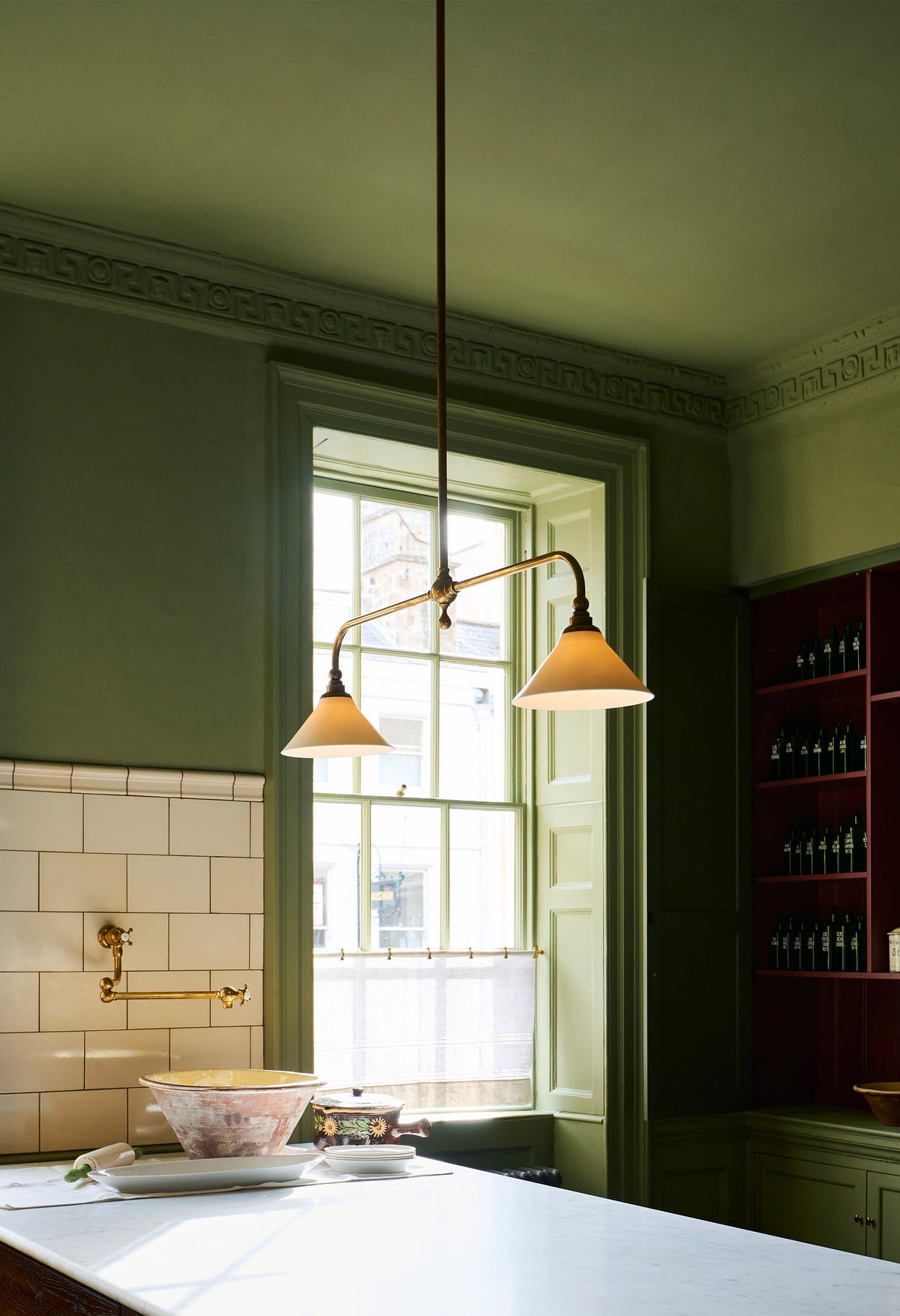 An oblique view of an Heirloom gaselier lights in a  quaint and stylish Wilkes green Heirloom kitchen features a large dairy table, creating a luxurious dining and social space.