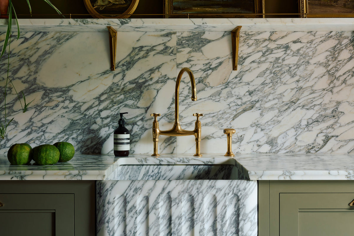 A close-up of an exquisite aged brass ionian tap, standing out against a marble counter top, splash back and shelf.