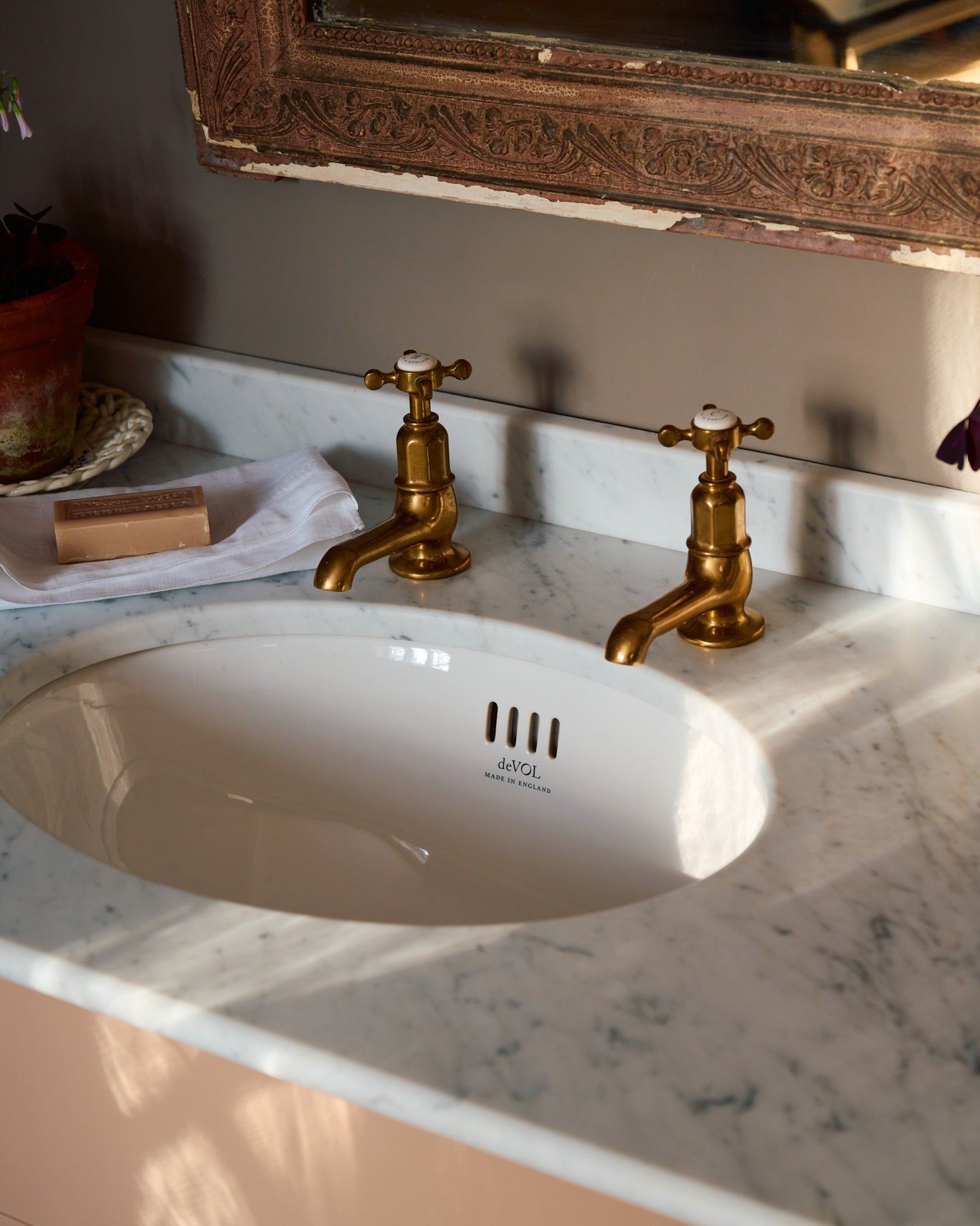 An oblique view of a pair of aged brass pillar taps with crosshead handles for a bathroom basin sink.