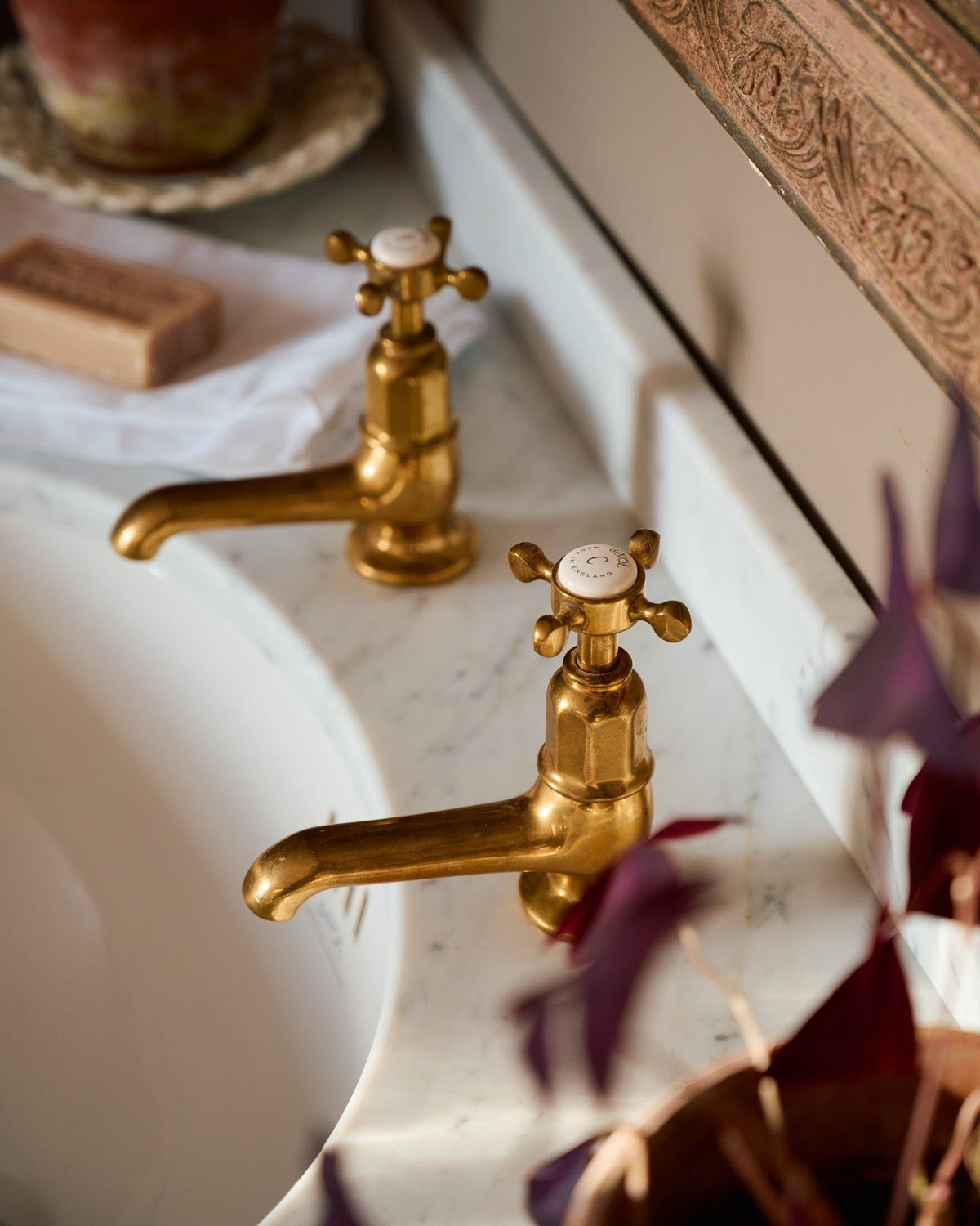 A close-up oblique view of a pair of aged brass pillar taps with crosshead handles for a bathroom basin sink. TEST