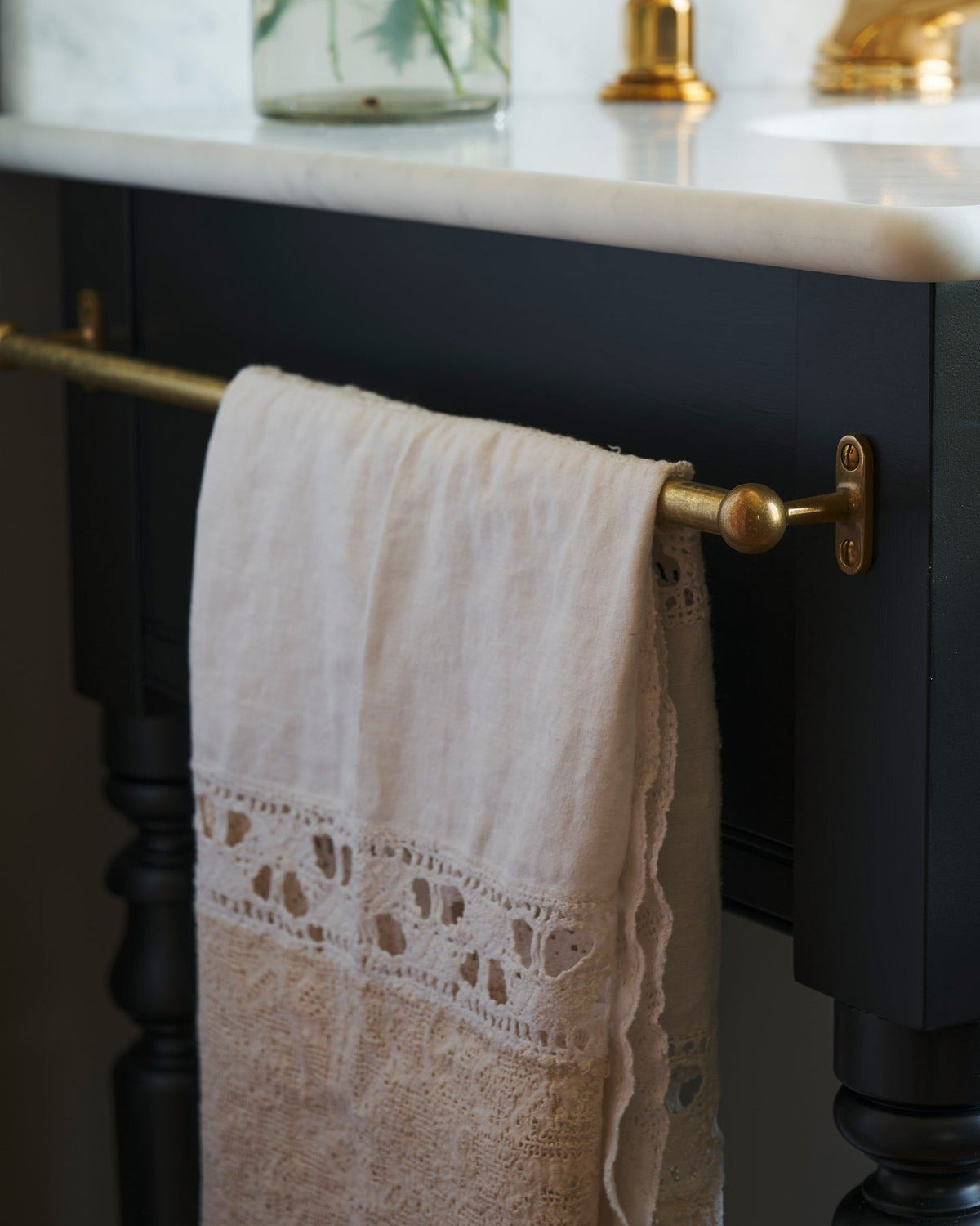 A detailed view of an aged brass towel rail attached to the left side of a Victorian-inspired washstand, a vintage lace hand towel hangs from the rail. | Left Towel Rail shown TEST