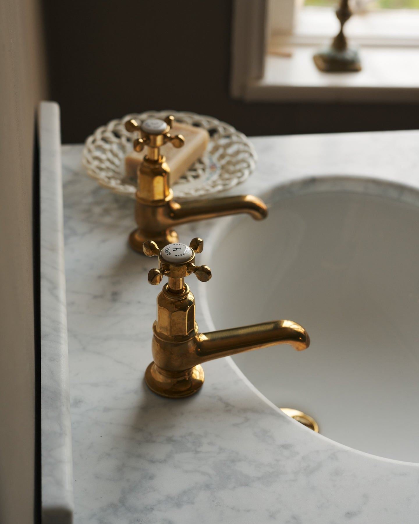 A profile view of a pair of aged brass pillar taps fitted to a bathroom washstand.
