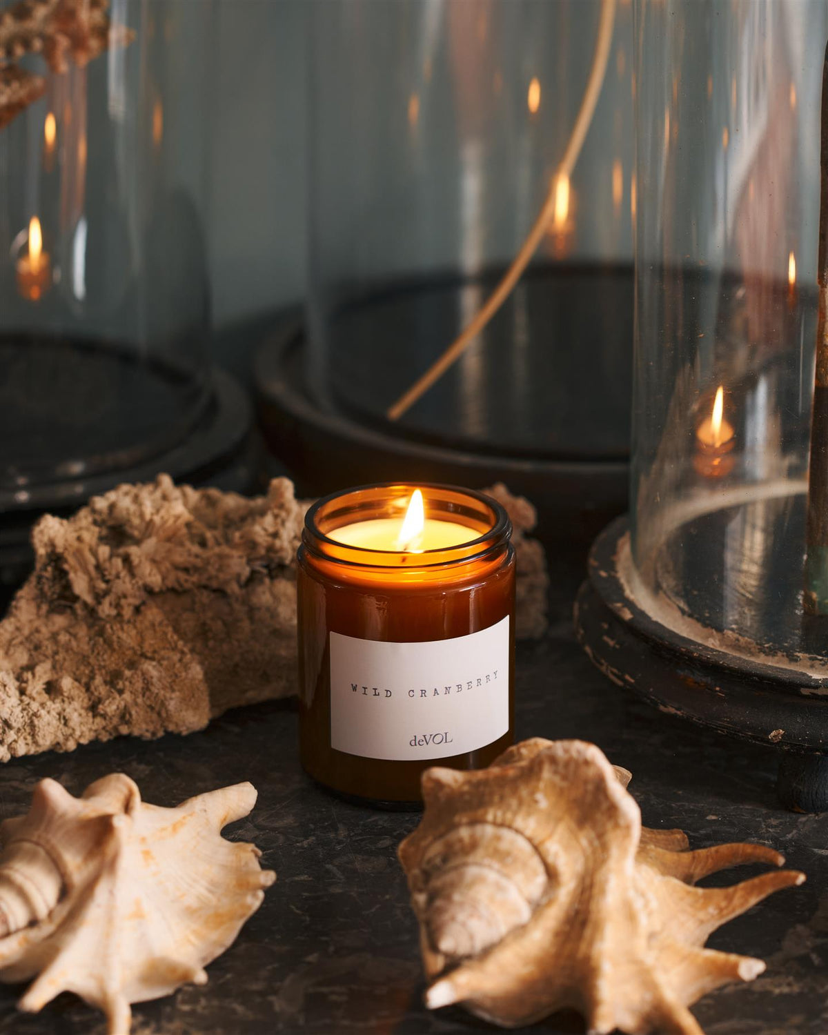 A lit medium scented candle in a brown glass jar with one wick, on a polished quartz worktop. TEST