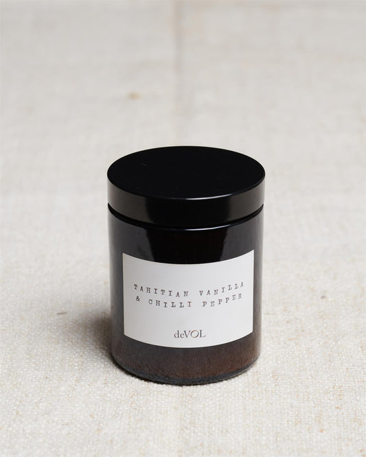 A medium scented candle in a brown glass jar with a black lid, the label reads 'Amber & Tonka Bean, deVOL'.