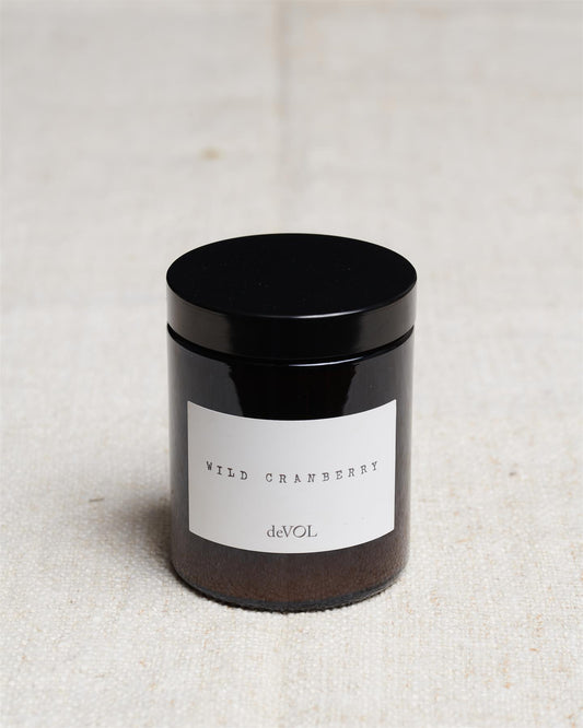 A medium scented candle in a brown glass jar with a black lid, the label reads 'Amber & Tonka Bean, deVOL'.