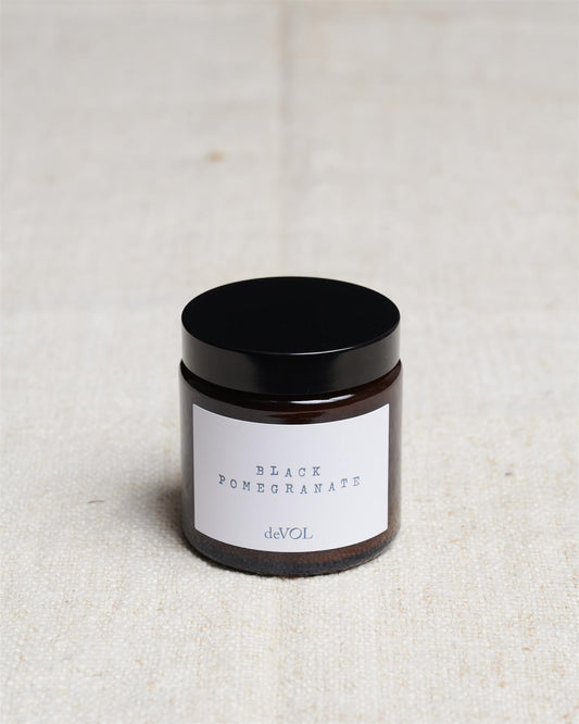 A small scented candle in a brown glass jar with a black lid, the label reads 'Amber & Tonka Bean, deVOL'.
