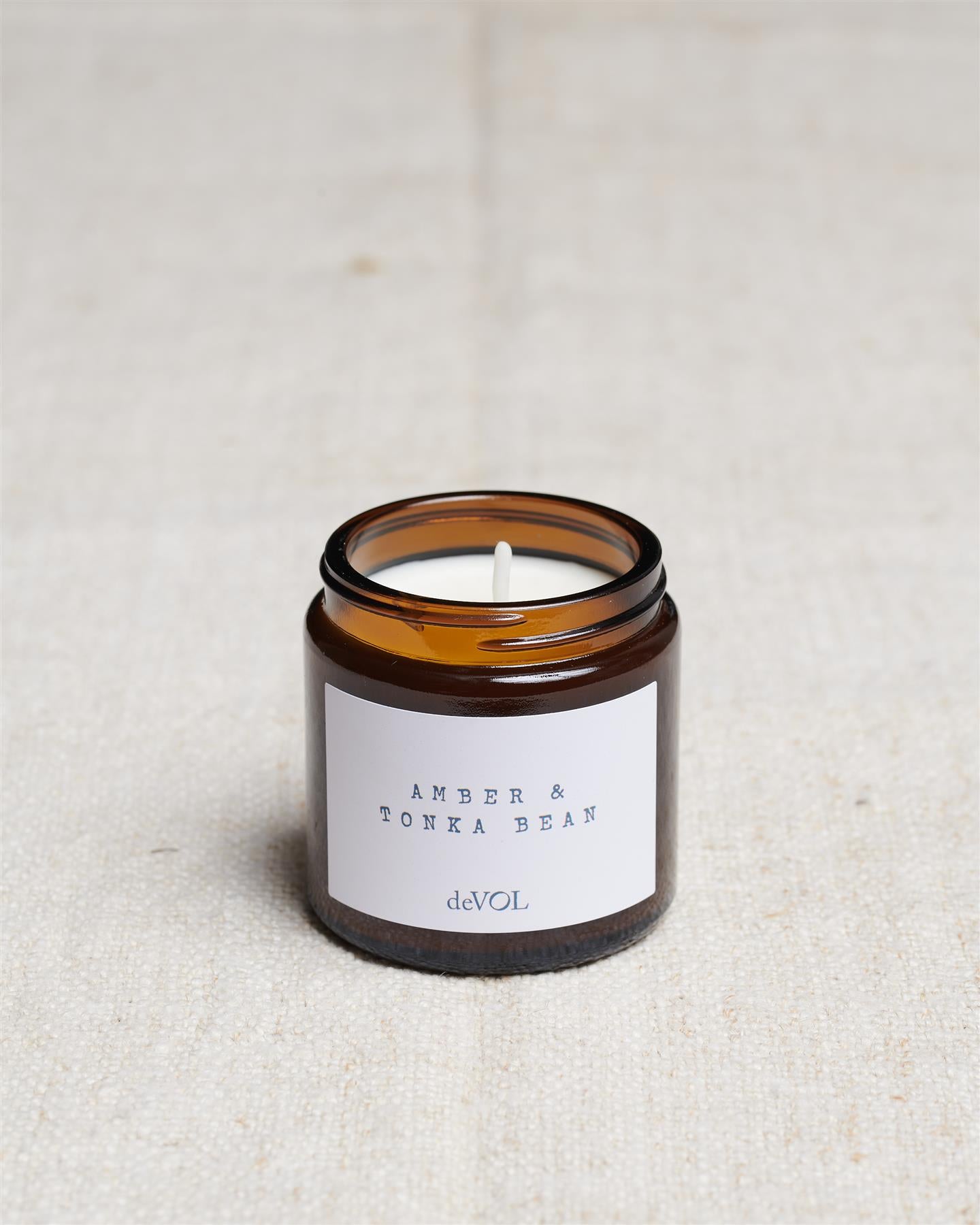 A collection of three lit scented candles in brown glass jars on a polished quartz worktop; small, medium and large.