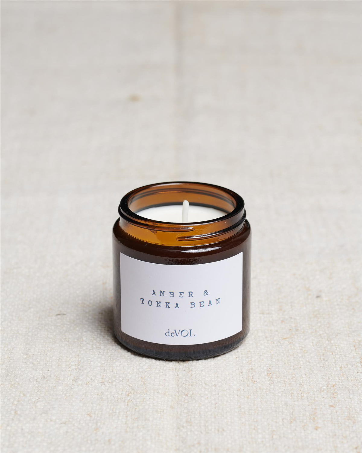 A collection of three lit scented candles in brown glass jars on a polished quartz worktop; small, medium and large. TEST