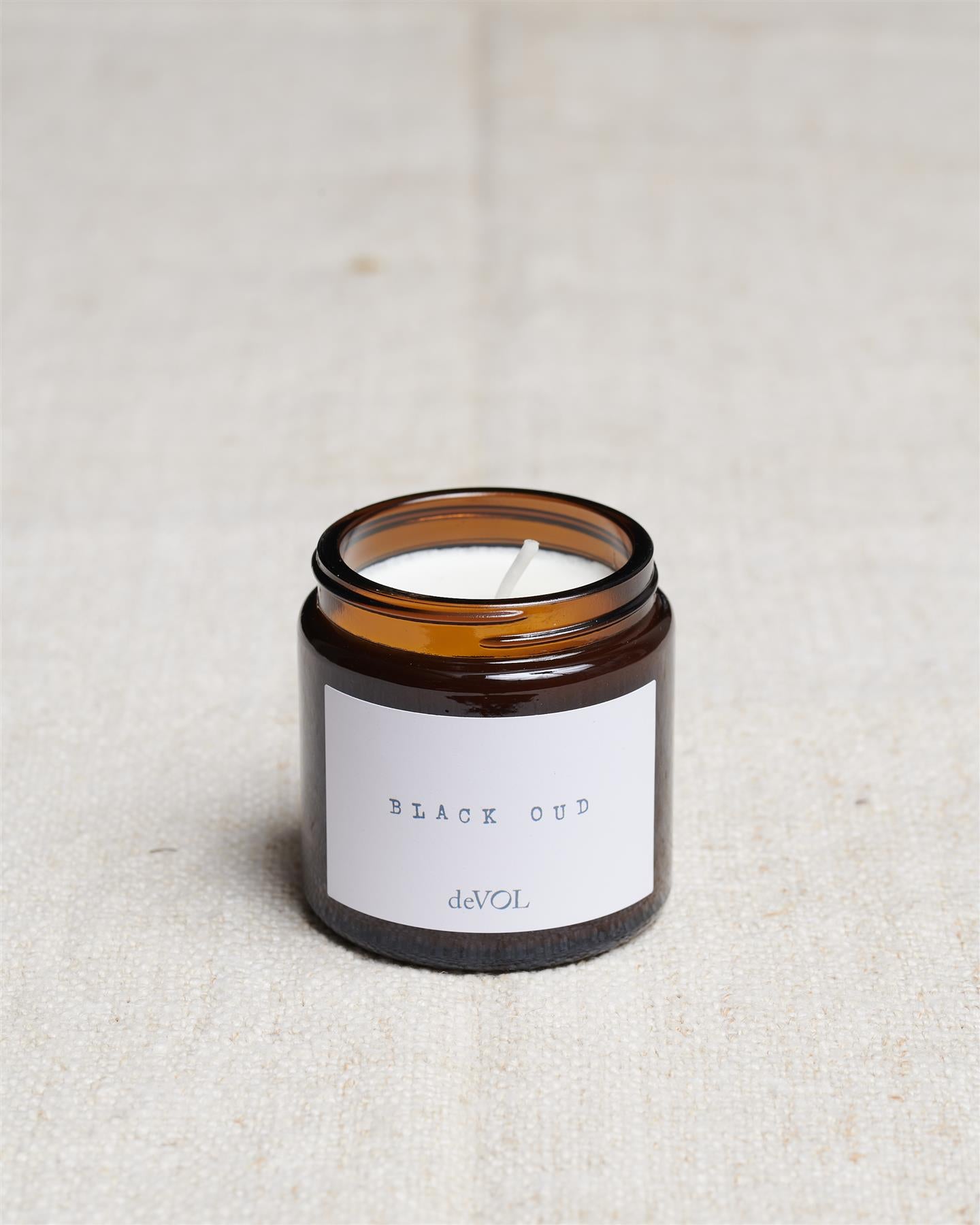 A collection of three lit scented candles in brown glass jars on a polished quartz worktop; small, medium and large.