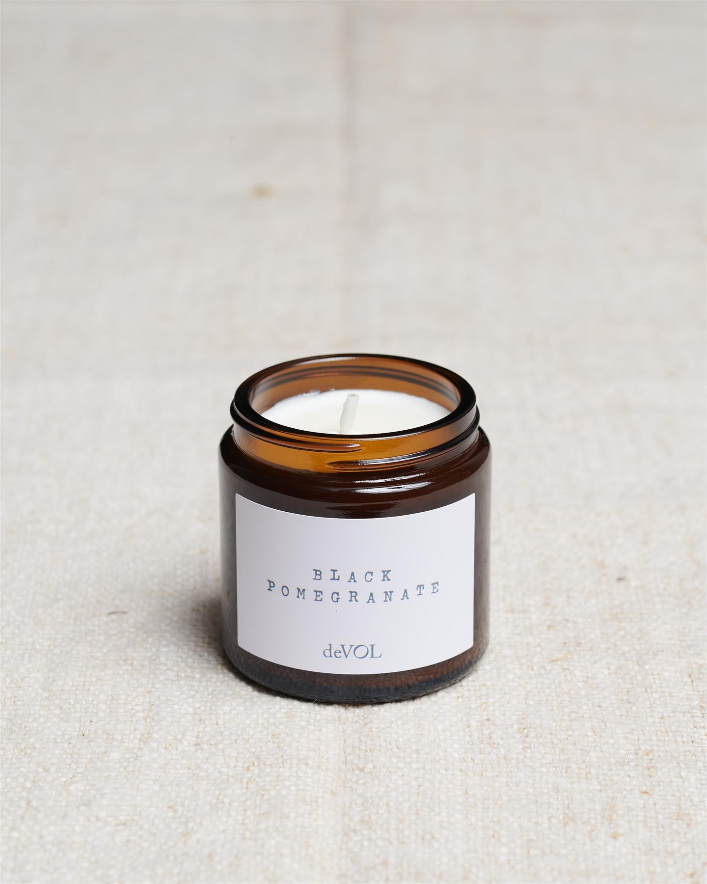 A collection of three lit scented candles in brown glass jars on a polished quartz worktop; small, medium and large.