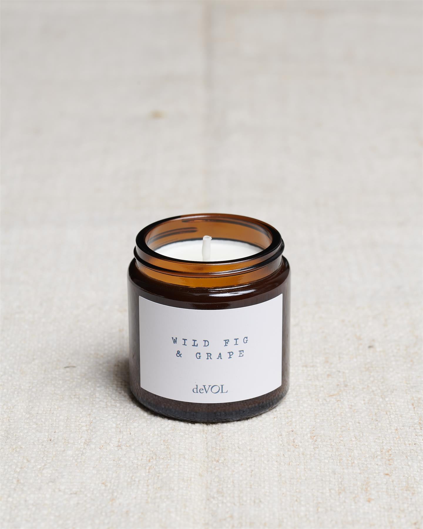 A collection of three lit scented candles in brown glass jars on a polished quartz worktop; small, medium and large.