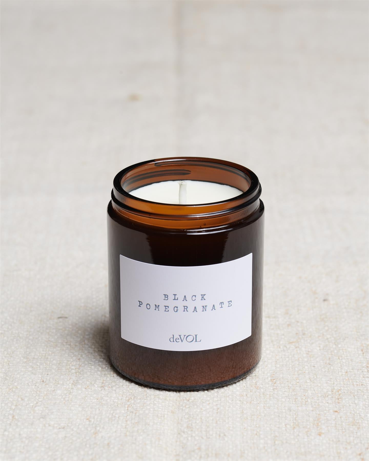 A collection of three lit scented candles in brown glass jars on a polished quartz worktop; small, medium and large.