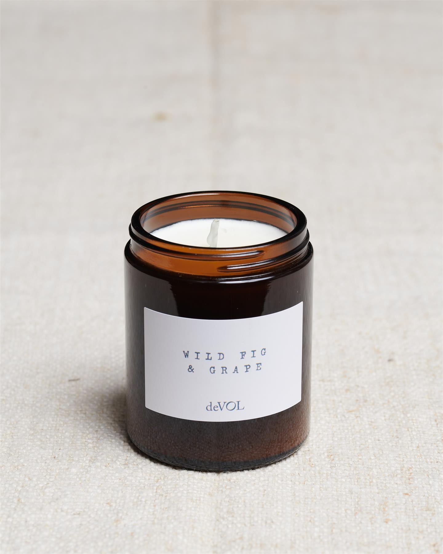 A collection of three lit scented candles in brown glass jars on a polished quartz worktop; small, medium and large.