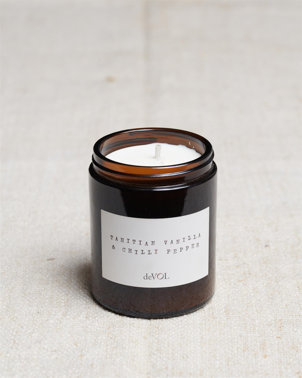 A collection of three lit scented candles in brown glass jars on a polished quartz worktop; small, medium and large. TEST