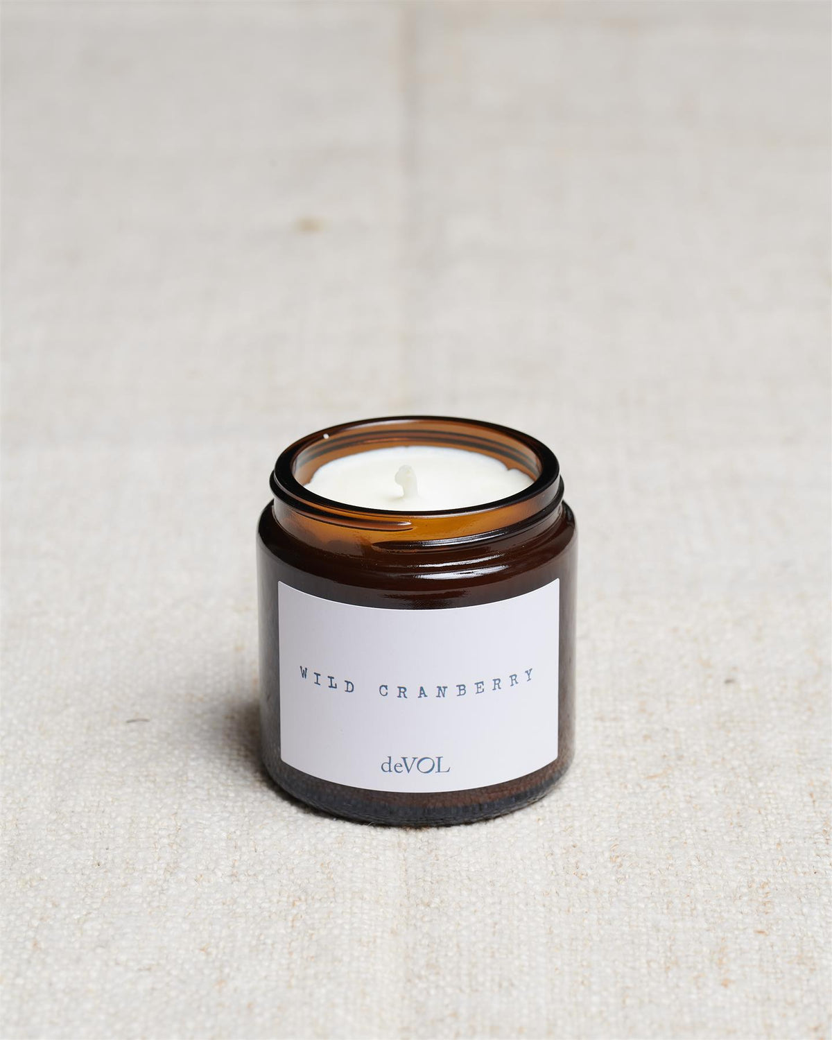 A collection of three lit scented candles in brown glass jars on a polished quartz worktop; small, medium and large. TEST