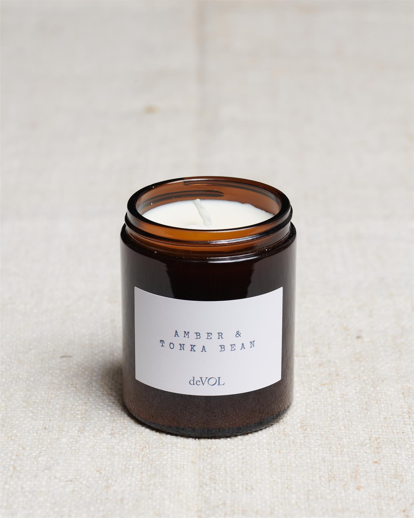 A collection of three lit scented candles in brown glass jars on a polished quartz worktop; small, medium and large.