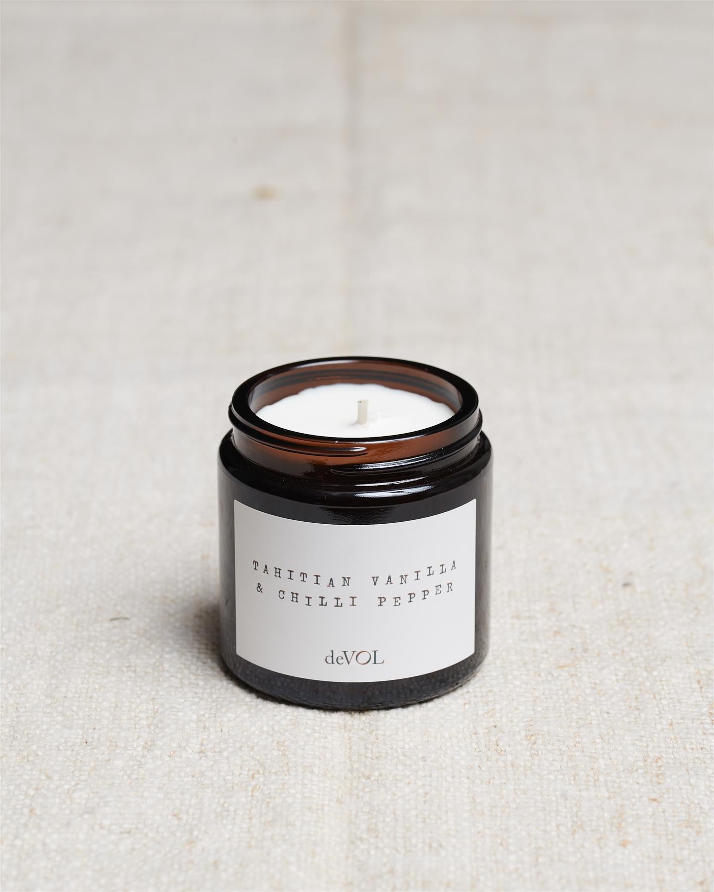A collection of three lit scented candles in brown glass jars on a polished quartz worktop; small, medium and large.