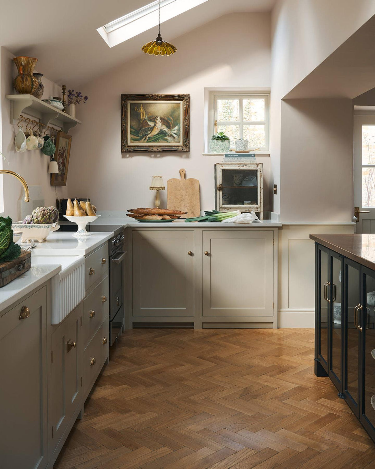 A straight-on view of a minimal room with white walls, a marble fireplace surround, fitted white painted Shaker-style cabinetry and oak parquet flooring with a warm aged finish. TEST
