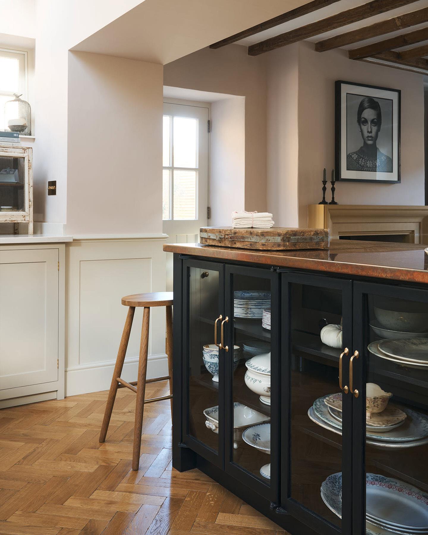 An oblique view of a minimal room with white walls, fitted white painted Shaker-style cabinetry and oak parquet flooring with a warm aged finish.