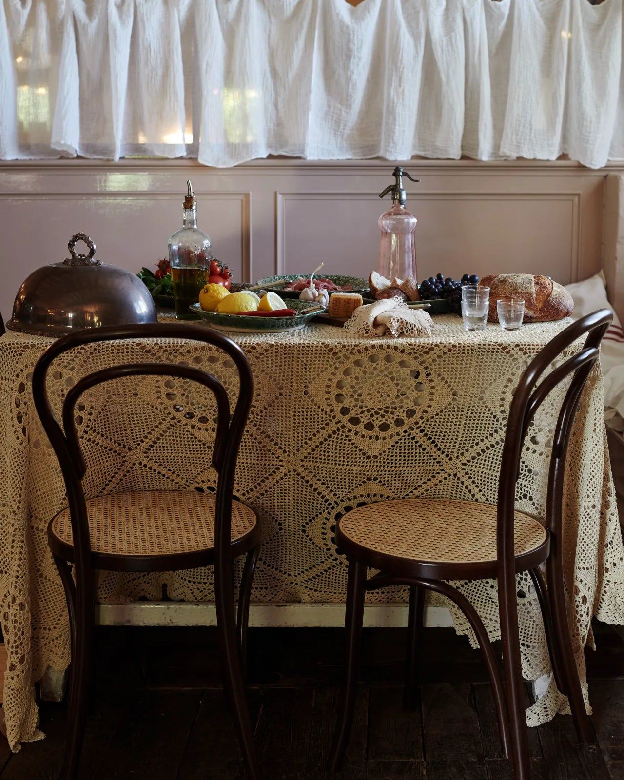 An oblique view of two cafÈ-style bar stools with dark stained frames and light woven ratten seats by a vintage table.