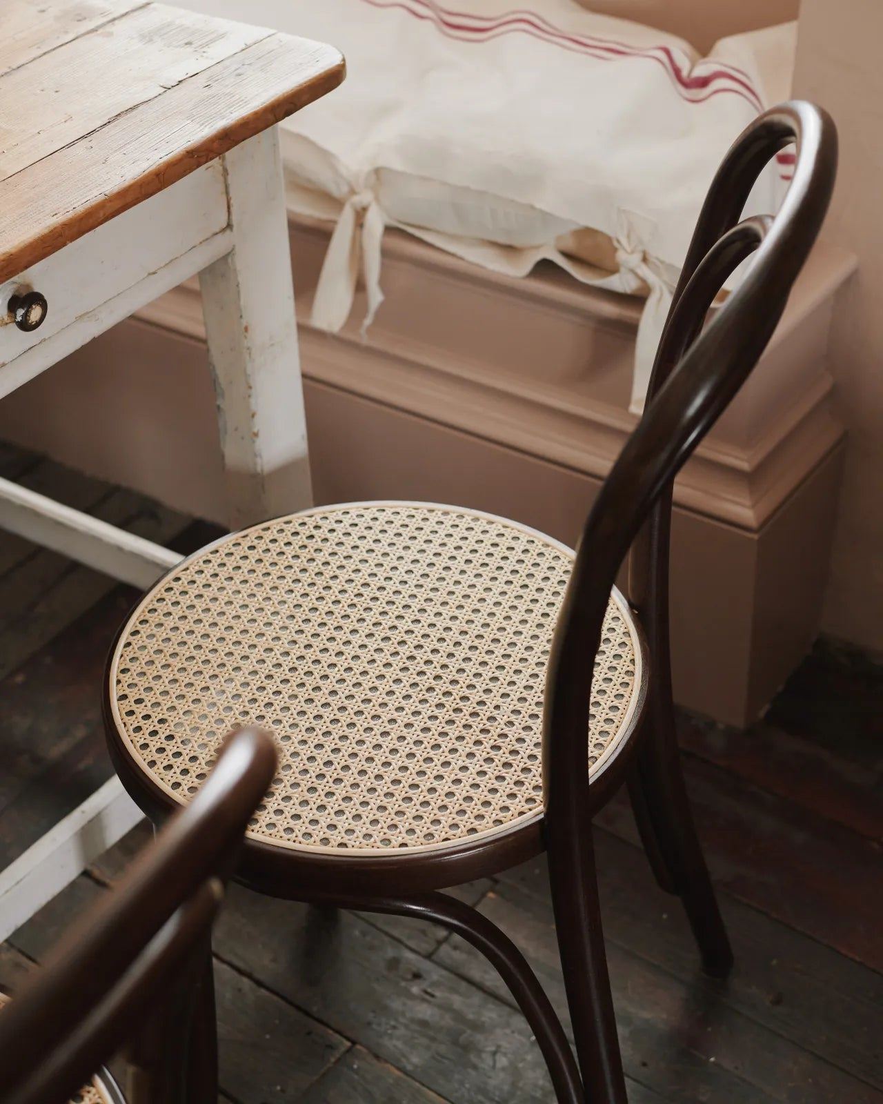A three-quarters profile view of a cafÈ-style bar stool with a dark stained frame and light woven ratten seat.