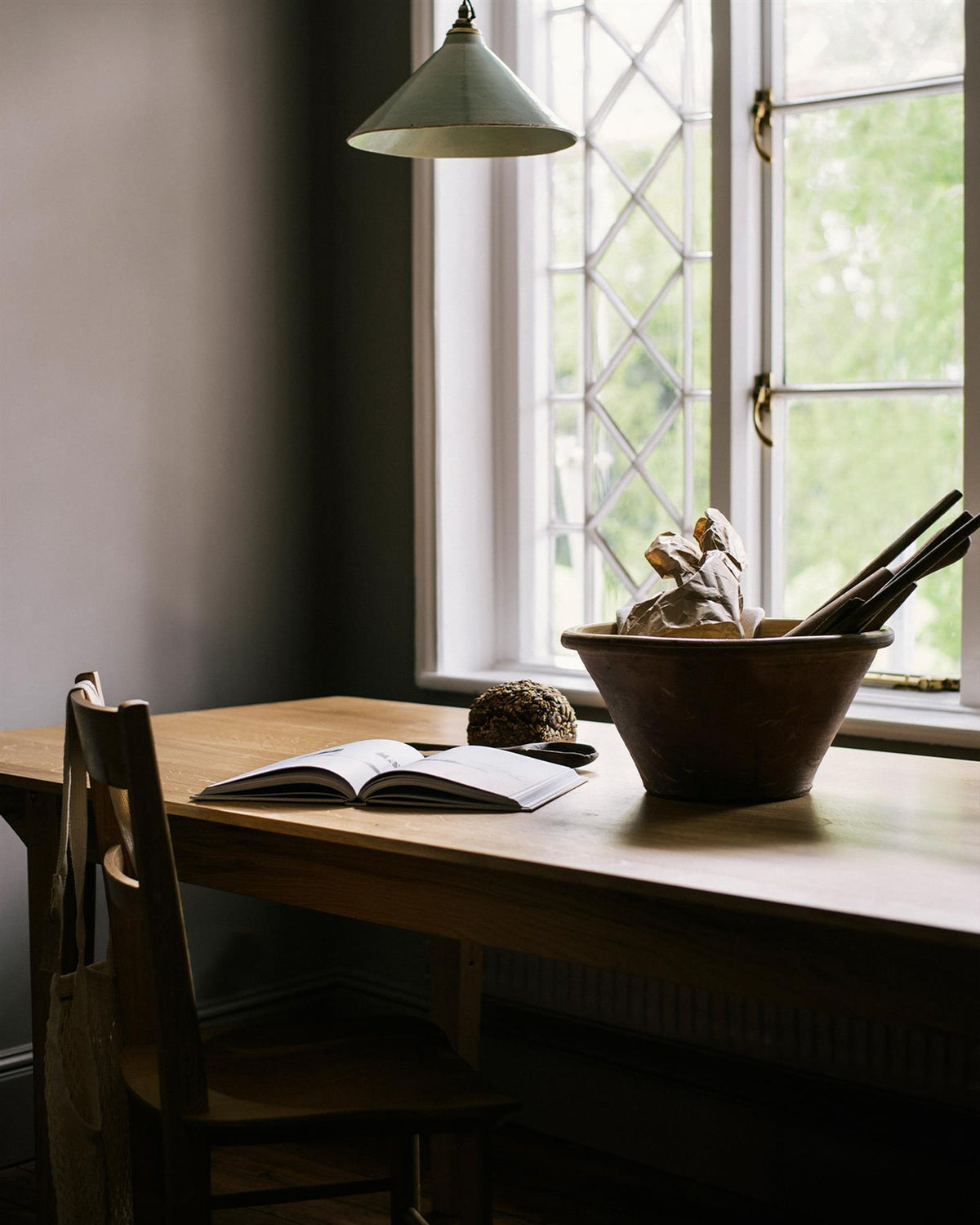 An oblique view of an oak tabletop with a large ceramic bowl in front of a Victorian leaded window. TEST