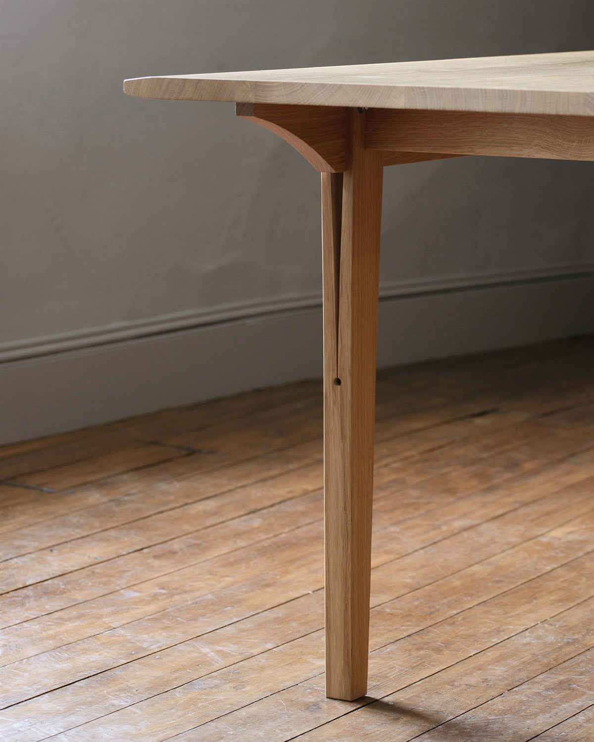 A close-up view of a chamfered oak table leg with a long split design which locks onto the table apron. TEST
