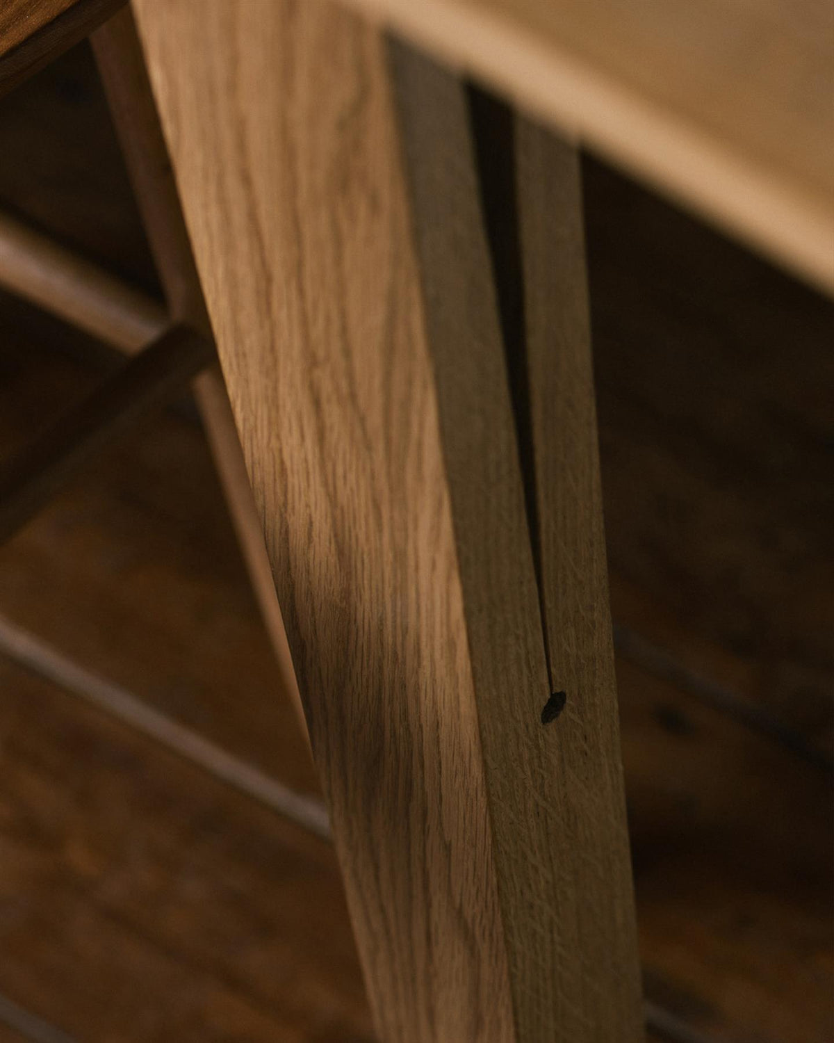 A close-up oblique view of a chamfered oak table leg with a long split design which locks onto the table apron. TEST