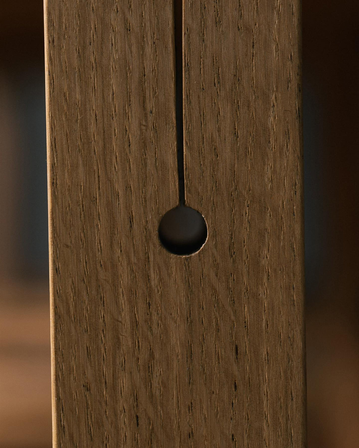 A close-up view of a circular hole at the base of a split design in an oak table leg. TEST