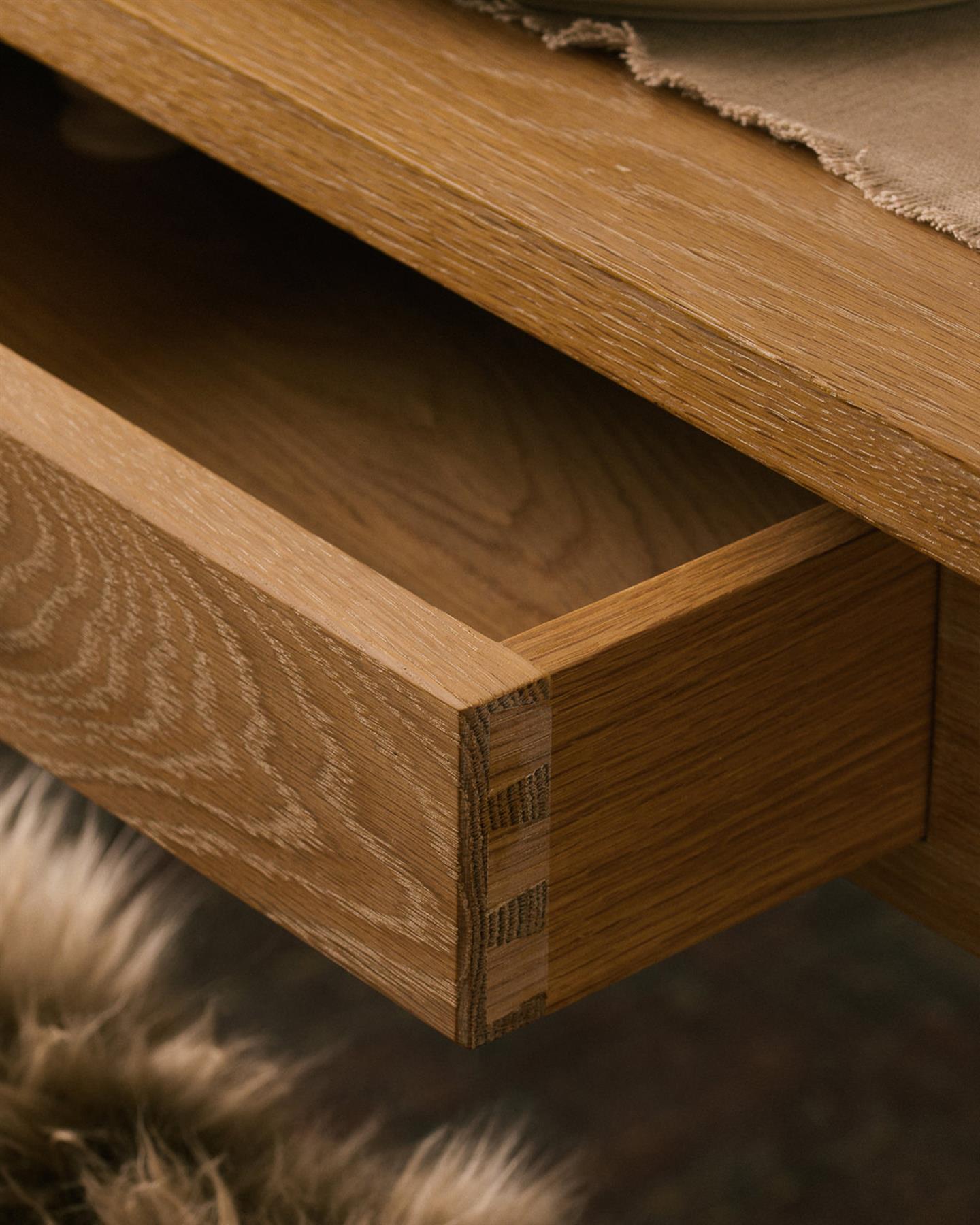 A close-up view of a shallow drawer in the apron of a Shaker-style oak dining table.