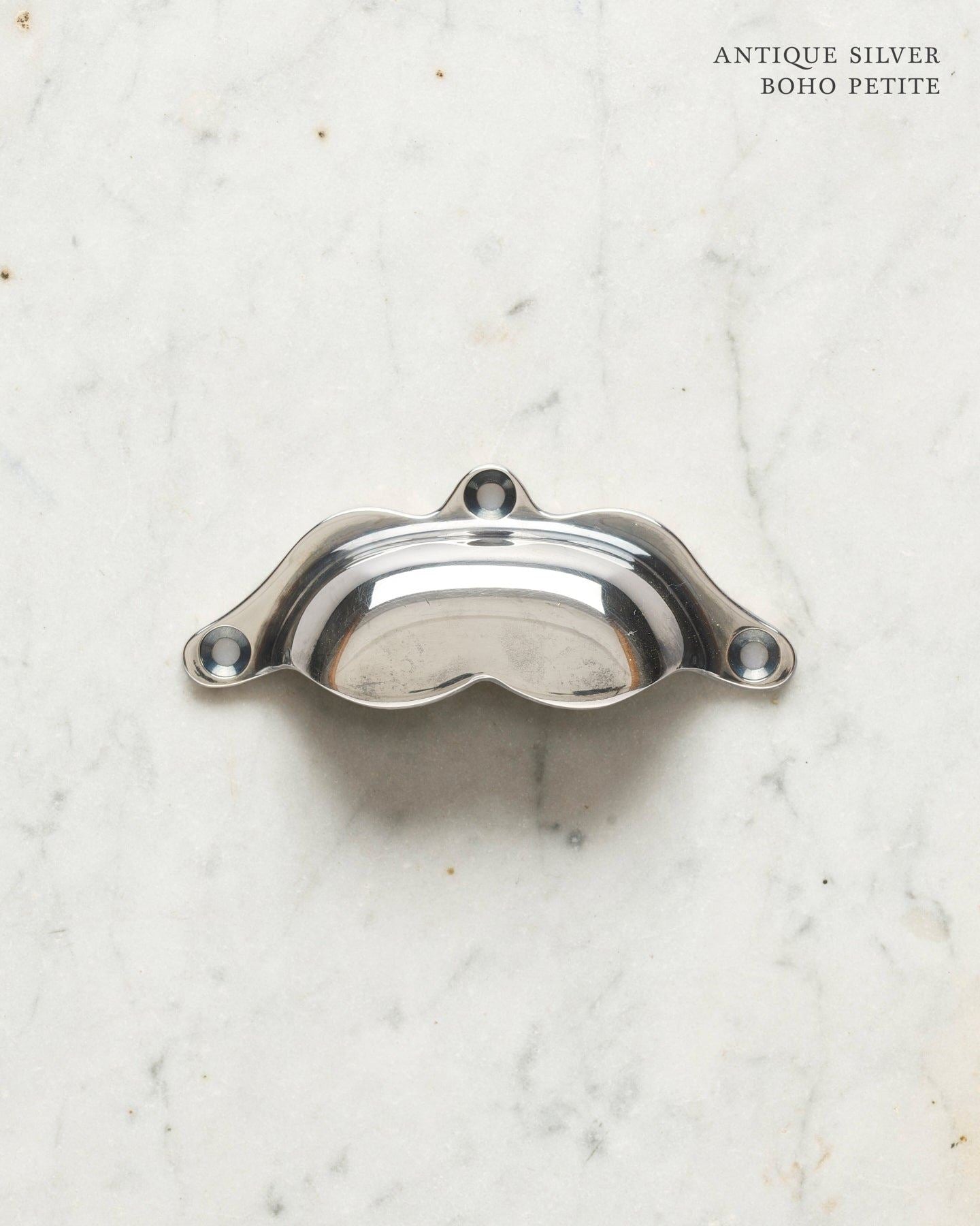 A small bohemian-style cup handle for a kitchen cupboard or drawer with a tarnished silver finish.